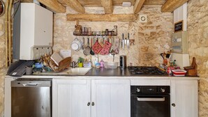 Una cocina rústica con paredes de piedra, vigas de madera, lavavajillas de acero inoxidable, estufa y diversos utensilios de cocina.