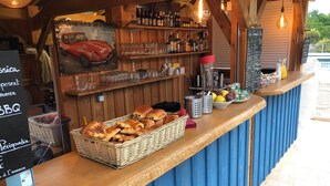 A rustic bar area with wooden shelves, a wicker basket of bread, and a variety of bottles and glasses. - Holiday Home 'Les Crouquets - La Grange' with Shared Terrace, Private Garden and Wi-Fi (Jayac)