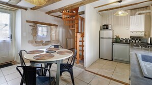 A kitchen with a wooden staircase, a dining table with woven placemats, and a modern refrigerator. - Holiday Home 'Les Crouquets - La Grange' with Shared Terrace, Private Garden and Wi-Fi (Jayac)
