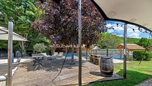 A wooden deck with outdoor furniture, a barbecue area, and a pool in the background. - Les Crouquets - Le cerisier (Jayac)