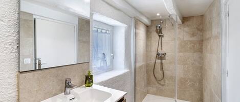 A bathroom with a large mirror, a sink, a shower, and a window.
