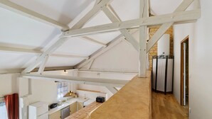 A high-ceilinged kitchen with exposed beams, a tiled backsplash, and a view of a bedroom through an open doorway. - Les crouquets - Le Pêcher (Jayac)