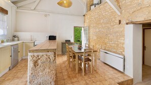 A kitchen with a stone wall, wooden dining table, and chairs. - Les crouquets - Le Pêcher (Jayac)