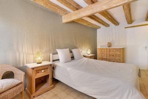 Une chambre à coucher avec un lit, des tables de chevet en bois, une commode, un fauteuil en osier et une lampe.