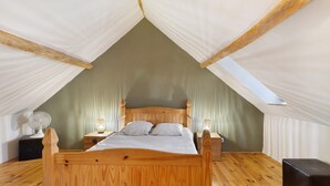 A wooden bed in a tent-like room with a sloped ceiling, a bedside table, and a lamp. - Les Crouquets - Le Fournil (Jayac)