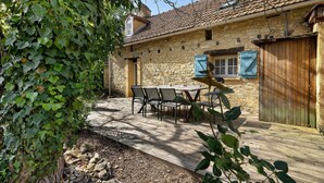 A stone building with a tiled roof, a wooden deck, and a table with chairs. - Les Crouquets - Le Fournil (Jayac)