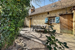 Un bâtiment en pierre avec un toit en tuiles, une terrasse en bois et une table entourée de chaises.