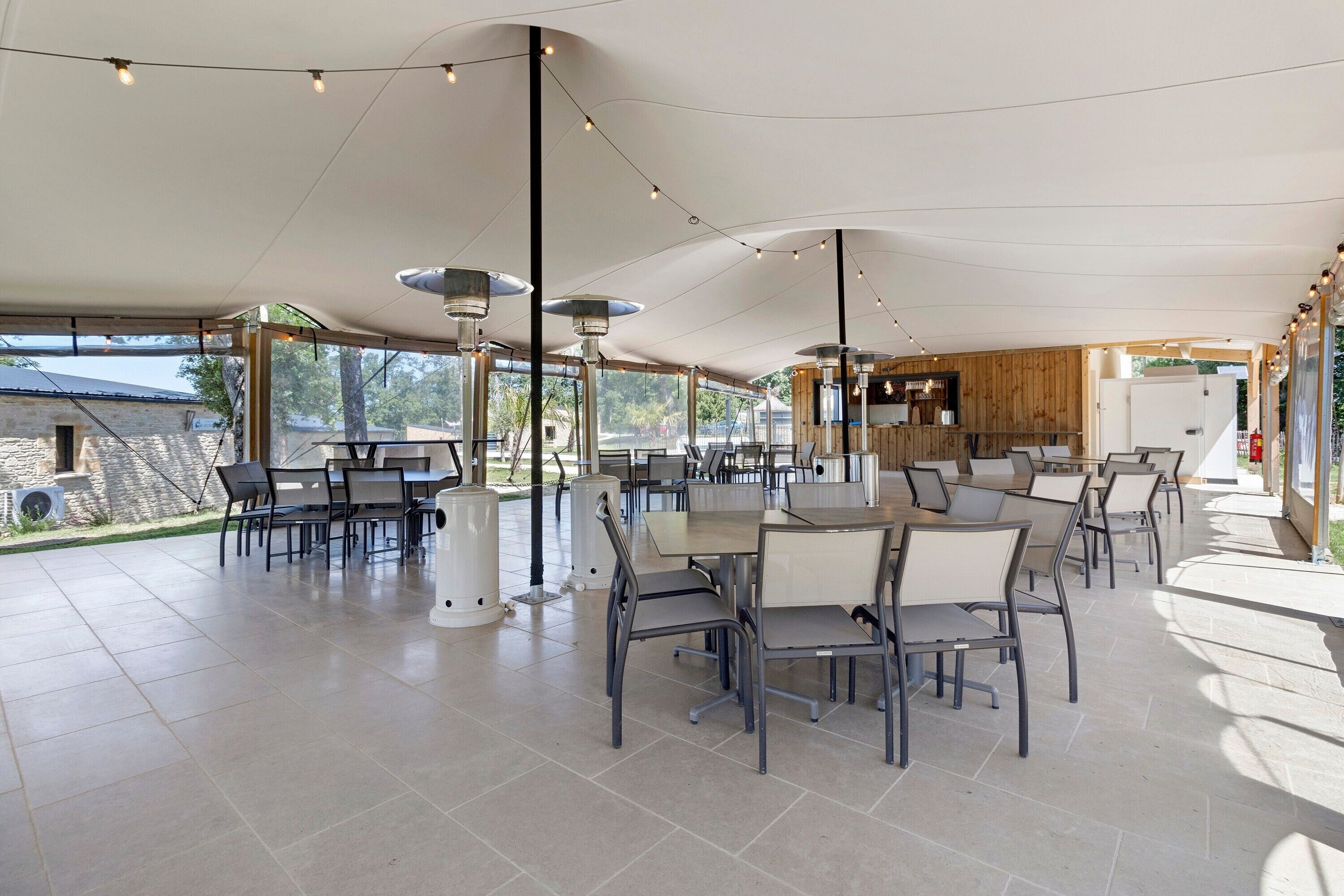 An outdoor dining area with tables and chairs, string lights, and a view of the surrounding landscape.