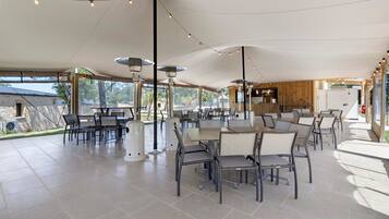 An outdoor dining area with tables and chairs, string lights, and a view of the surrounding landscape.