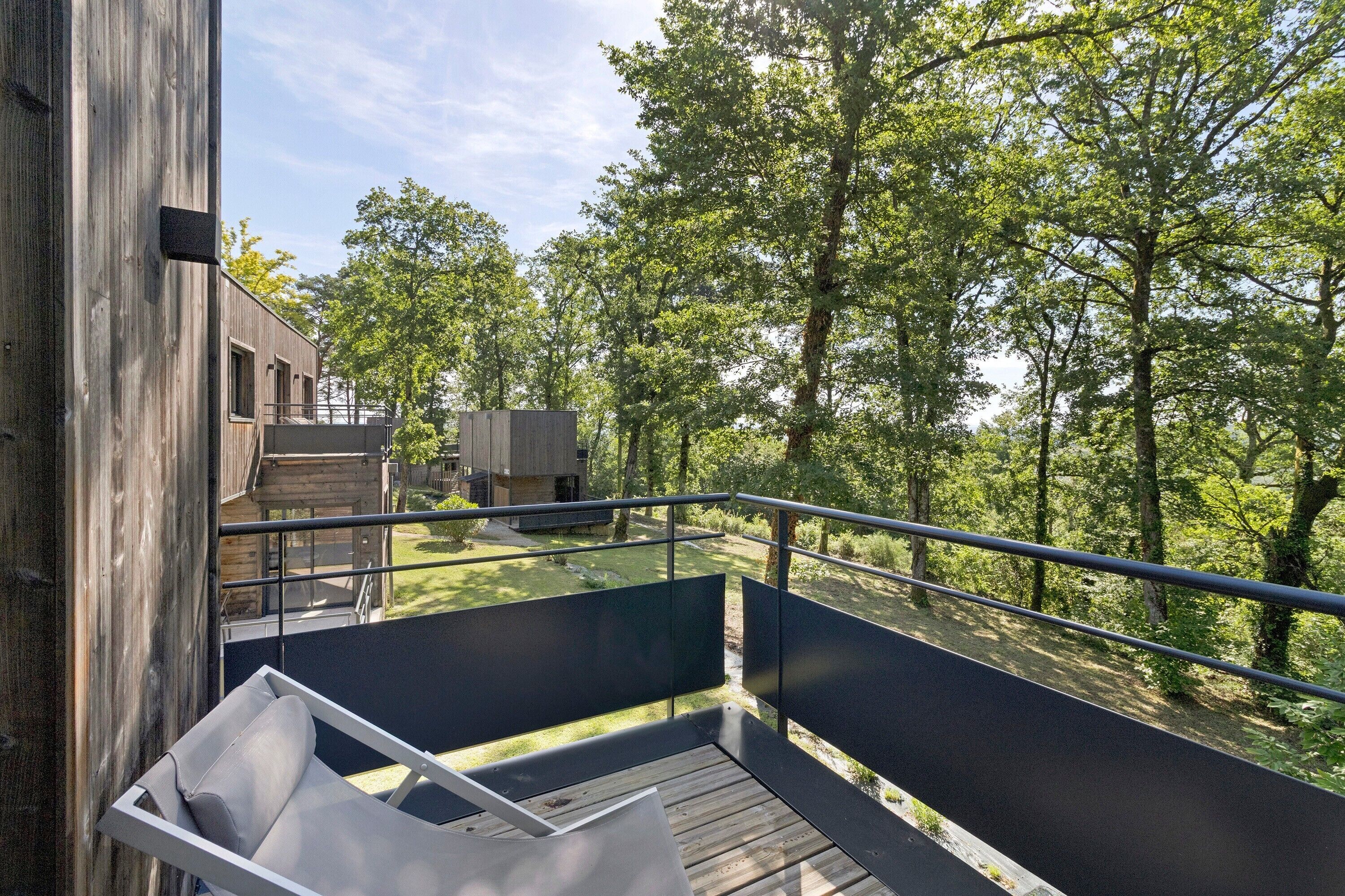 A wooden deck with a metal railing overlooking a forested area.