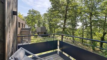 A wooden deck with a metal railing overlooking a forested area.