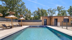 A swimming pool with lounge chairs and umbrellas, a wooden building with a sign, and a stone wall.