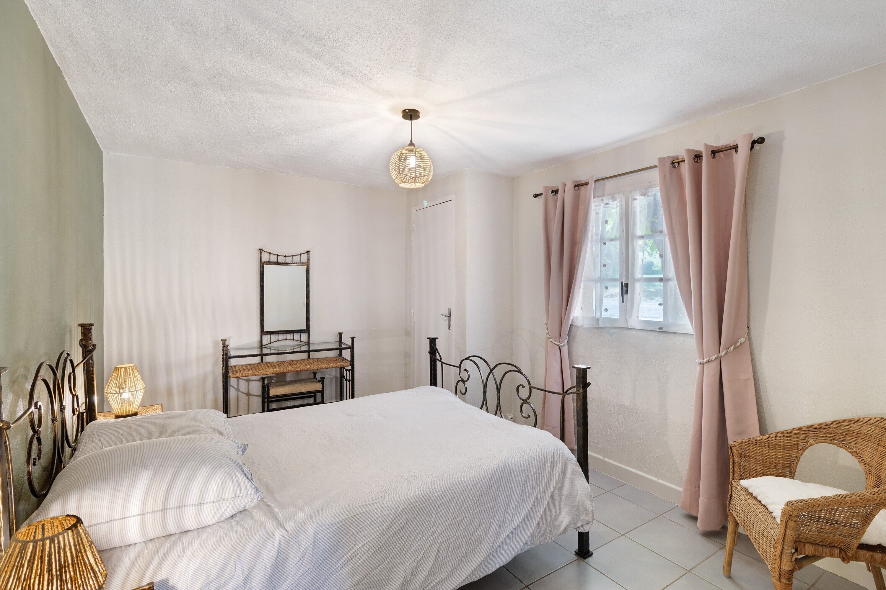 Een slaapkamer met een bed, nachtlampjes, een dressoir, een stoel en een raam met gordijnen.