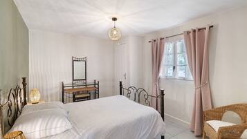 Een slaapkamer met een bed, nachtlampjes, een dressoir, een stoel en een raam met gordijnen.