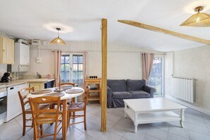 A modern kitchen with white cabinets, a dining table with chairs, a sofa, and a white coffee table. - Les crouquets - Le logis (Jayac)