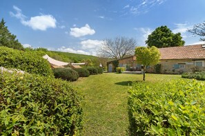 A well-maintained garden with a stone building, a tree, and a clear sky. - Les crouquets - Le logis (Jayac)