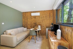 A modern living room with a sofa, a dining table with chairs, a TV, and a large window.
