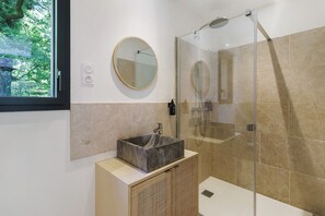 Une salle de bain moderne avec une douche à l’italienne en verre, un miroir rond et un lavabo rectangulaire.