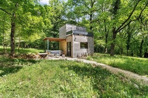 A small wooden cabin with a patio area, a grill, and a covered seating space.