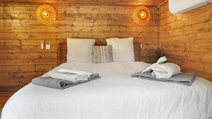 Une pièce aux murs lambrés, comprenant un lit, deux lampes fixées au mur et un appareil de climatisation.