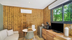 Une cuisine moderne avec un mur en bois, un coin repas avec une table et des chaises blanches, un canapé et une grande fenêtre donnant sur les arbres.