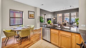 A modern kitchen with wooden cabinets, a stainless steel dishwasher, and a dining area with a round table and chairs. - Playhouse Square Condo /  Free Parking / Downtown (Cleveland)