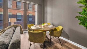Een eetruimte met een ronde tafel, gele stoelen en een grijze bank.