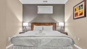 Hotelkamer met een groot bed, twee nachtkastjes, een wandairconditioning en een lijst met een abstract schilderij.