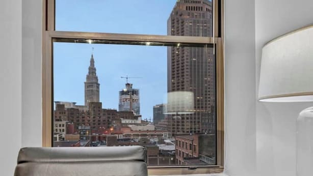 Una habitación moderna con un amplio ventanal que ofrece vistas a la ciudad, un sillón de cuero y una mesa de madera.