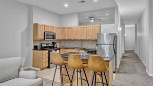 Una cocina funcional con armarios de madera, un refrigerador de acero inoxidable y un comedor con cuatro taburetes.