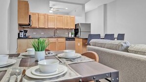 Eine moderne Küche mit Holzschränken, einem Esstisch mit weißen Tellern und Schüsseln, und einem grauen Sofa im Hintergrund.
