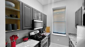 A kitchen with grey cabinets, a microwave, a stove, and a window with blinds. - Exquisite 1st Floor One Bedroom in Historic Marble Hill w/ Modern Amenities (Baltimore)