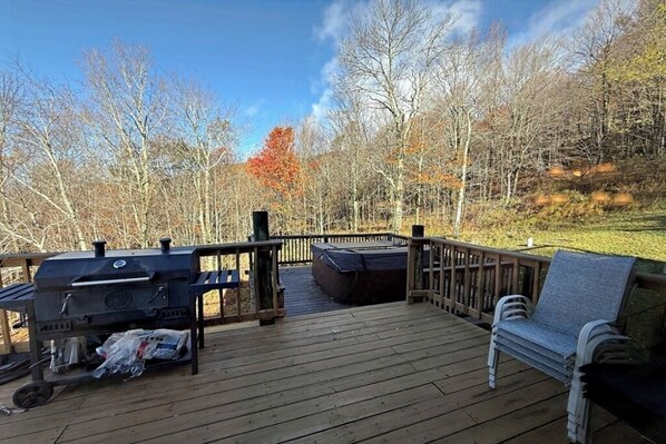 A wooden deck with a grill, hot tub, and a bench.
