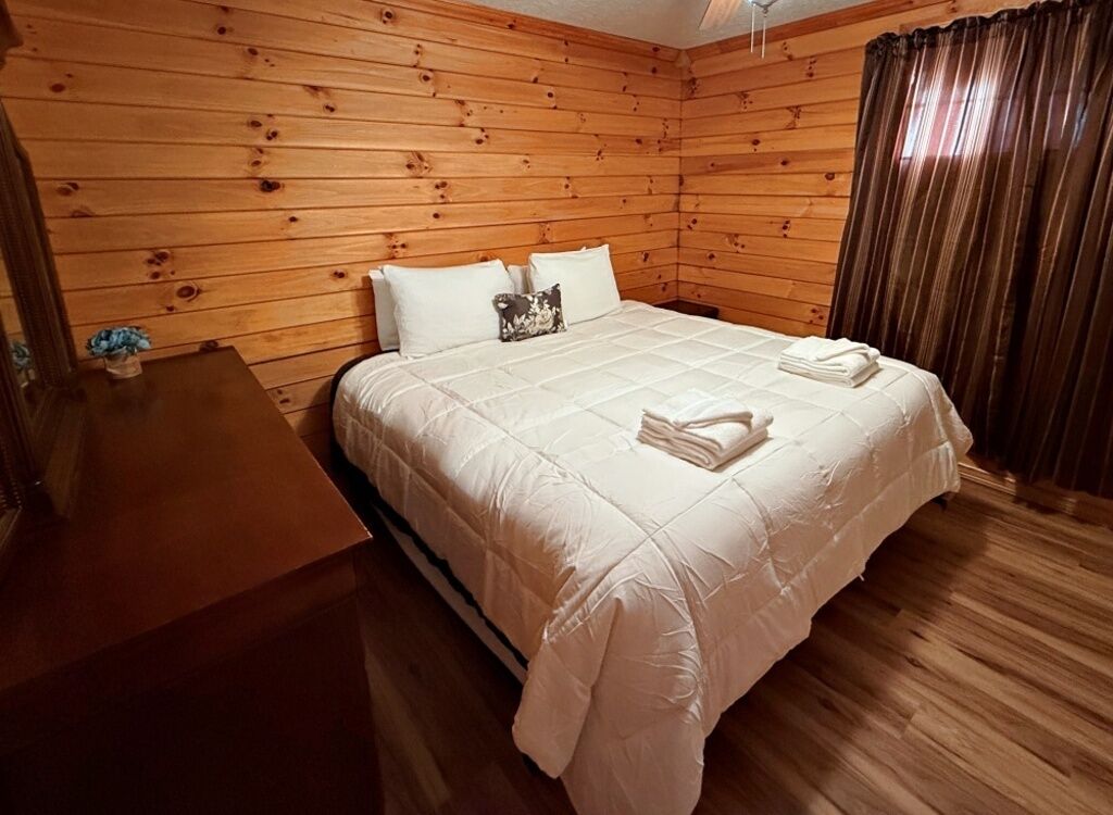 A wooden-paneled bedroom with a bed, pillows, and a small table with a vase.