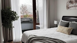 Un dormitorio moderno con una cama grande, una planta en maceta y vistas a través de un gran ventanal corredera.