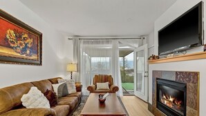 Una sala de estar con un sofá de cuero, una mesa de centro de madera, una chimenea y un televisor montado en la pared.
