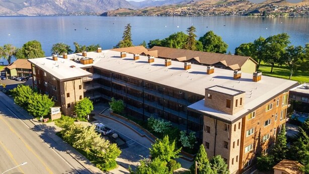 Un edificio de varios pisos con techo plano, rodeado de árboles y un lago.