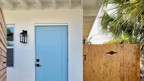 Una porta blu chiara con una maniglia nera e un lampione nero appeso al muro accanto.