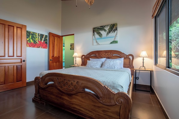 Una cama de madera con cabecera, dos lámparas de noche, un cuadro de una playa y una puerta a la izquierda.