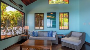 A living room with a sofa, a coffee table, and a wicker chair. There are three windows with views of greenery. - Breathtaking views on the pacific ocean - inifnity edge pool (Dominicalito)