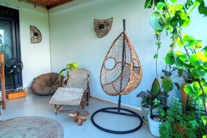 A cozy patio area with wicker furniture, a hanging chair, and potted plants.