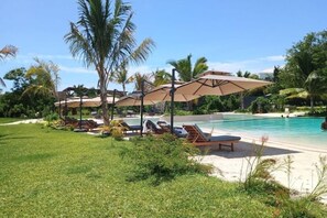 A poolside area with lounge chairs and umbrellas, surrounded by palm trees and greenery.