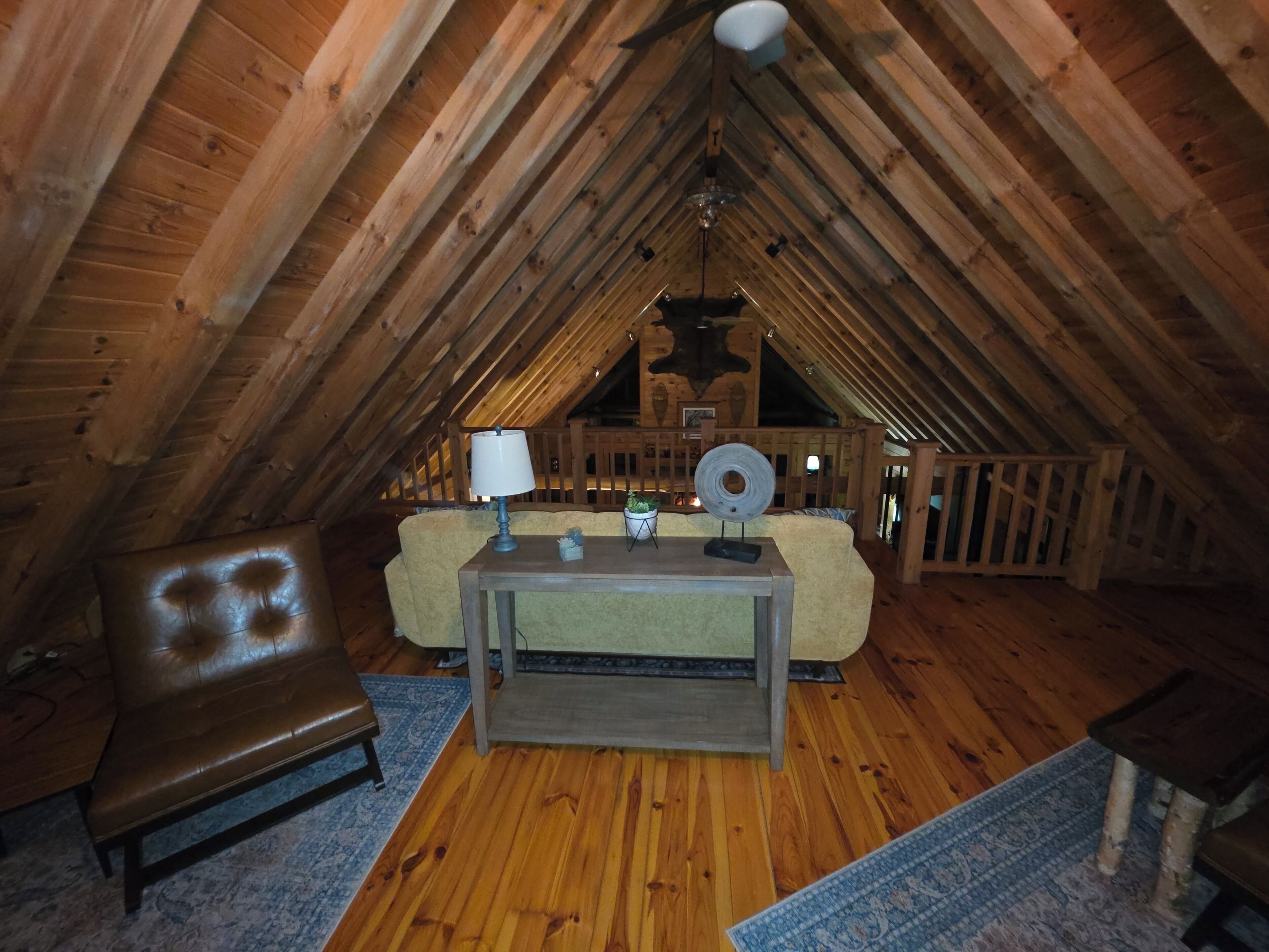 An attic room with wooden beams, a leather chair, a sofa, a small table with a lamp, and a rug.