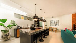 A modern kitchen with a central island, bar stools, pendant lighting, and a dining area with a teal sofa.
