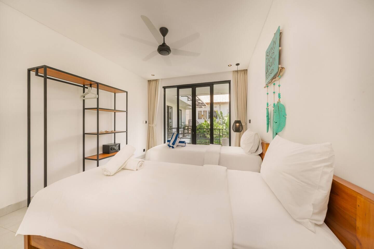 Une chambre avec un grand lit, une armoire avec des étagères, un ventilateur de plafond et une vue sur l’extérieur grâce à une porte vitrée.