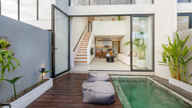 Ein modernes Haus mit Holzterrasse, kleinem Pool und einer Treppe zu einem offenen Wohnbereich.