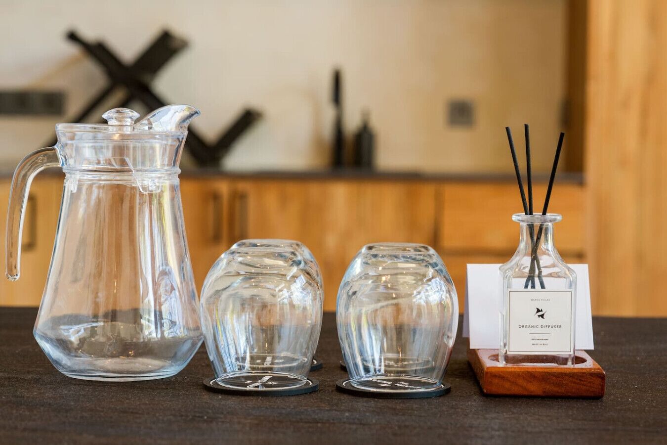 A kitchen counter with a glass pitcher, two glass vases, and a diffuser on a coaster.