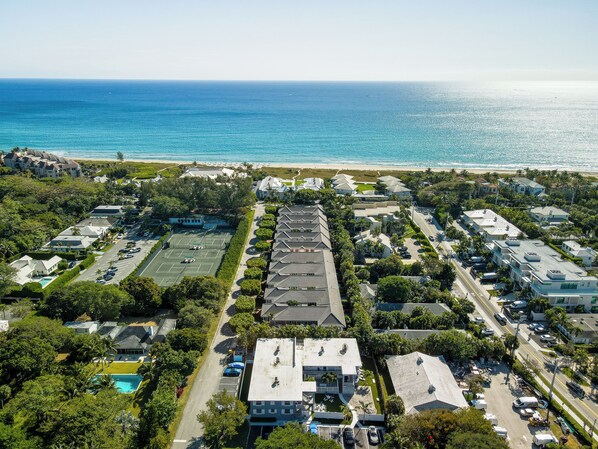 Vista aérea de una zona residencial costera con casas, una cancha de tenis y una playa al fondo.