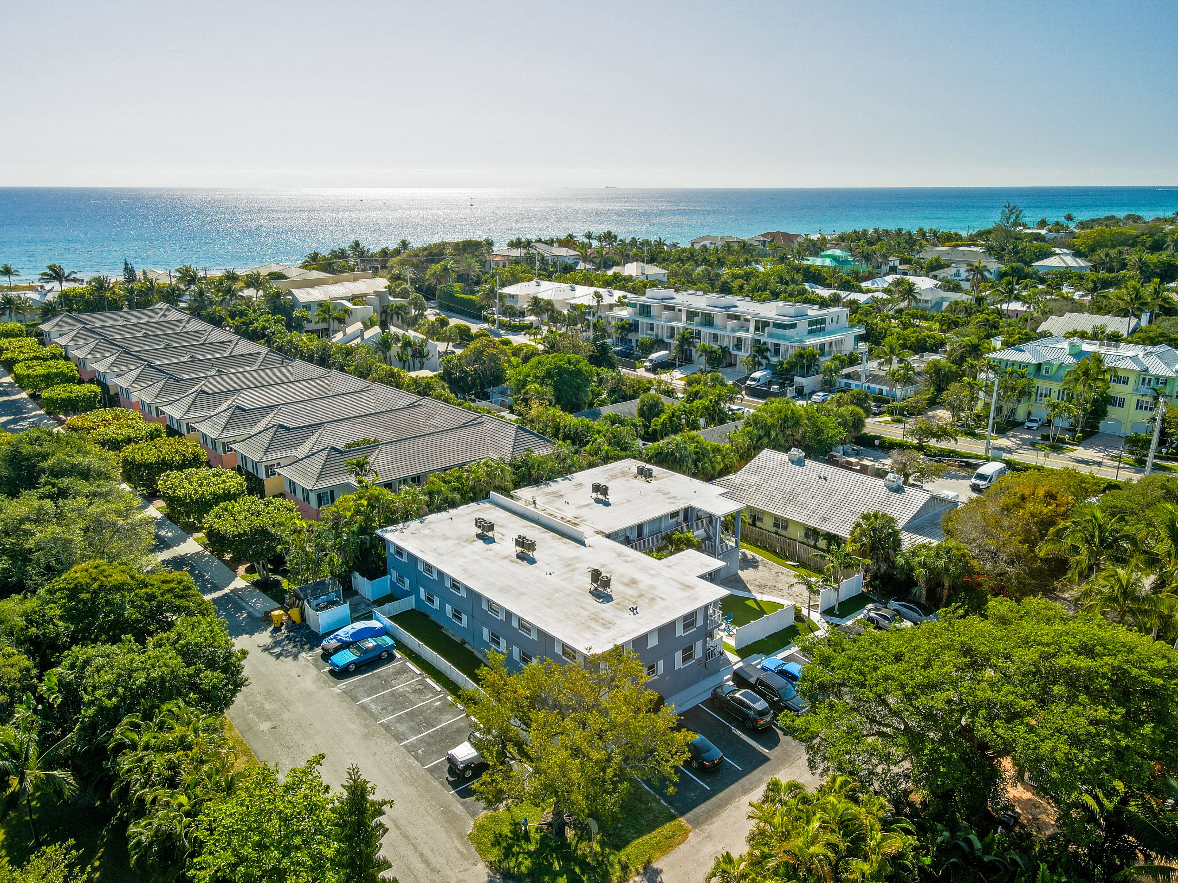 Una vista aerea di una zona residenziale costiera con diversi edifici, un parcheggio e una spiaggia con vista sull'oceano.