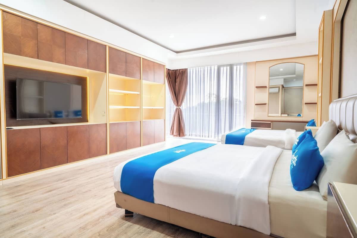 Una habitación de hotel moderna con una cama grande, un televisor montado en la pared y un ventanal con cortinas.
